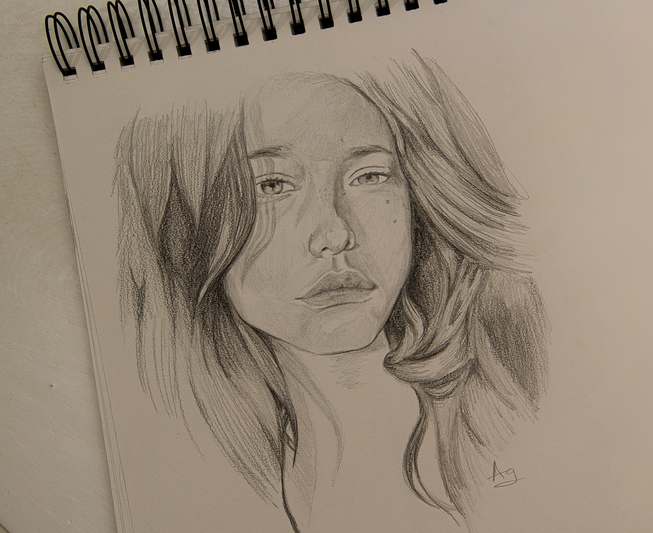 Hand holding a sketch pencil over an open, lightly shaded sketchbook with visible gesture lines and coffee cup in background